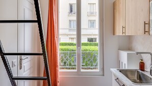 A kitchen with a window, white cabinets, a stainless steel sink, and a wooden cabinet. - Studio 2P - Roland Garros Stadium and Bois de Boulogne (Paris)