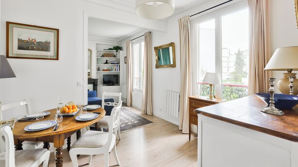 Een eetruimte met een houten tafel, witte stoelen, een kroonluchter en uitzicht op het buiten.