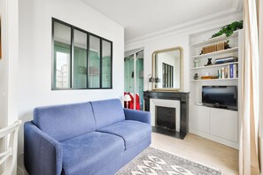 Ein Wohnzimmer mit einem blauen Sofa, einem Kamin, einem Fernseher und einem Bücherregal.