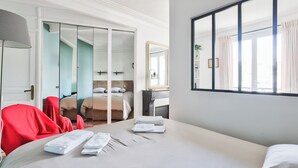Een hotelkamer met een bed, een rode stoel, een spiegel en een uitzicht op een stadsbeeld door het raam.