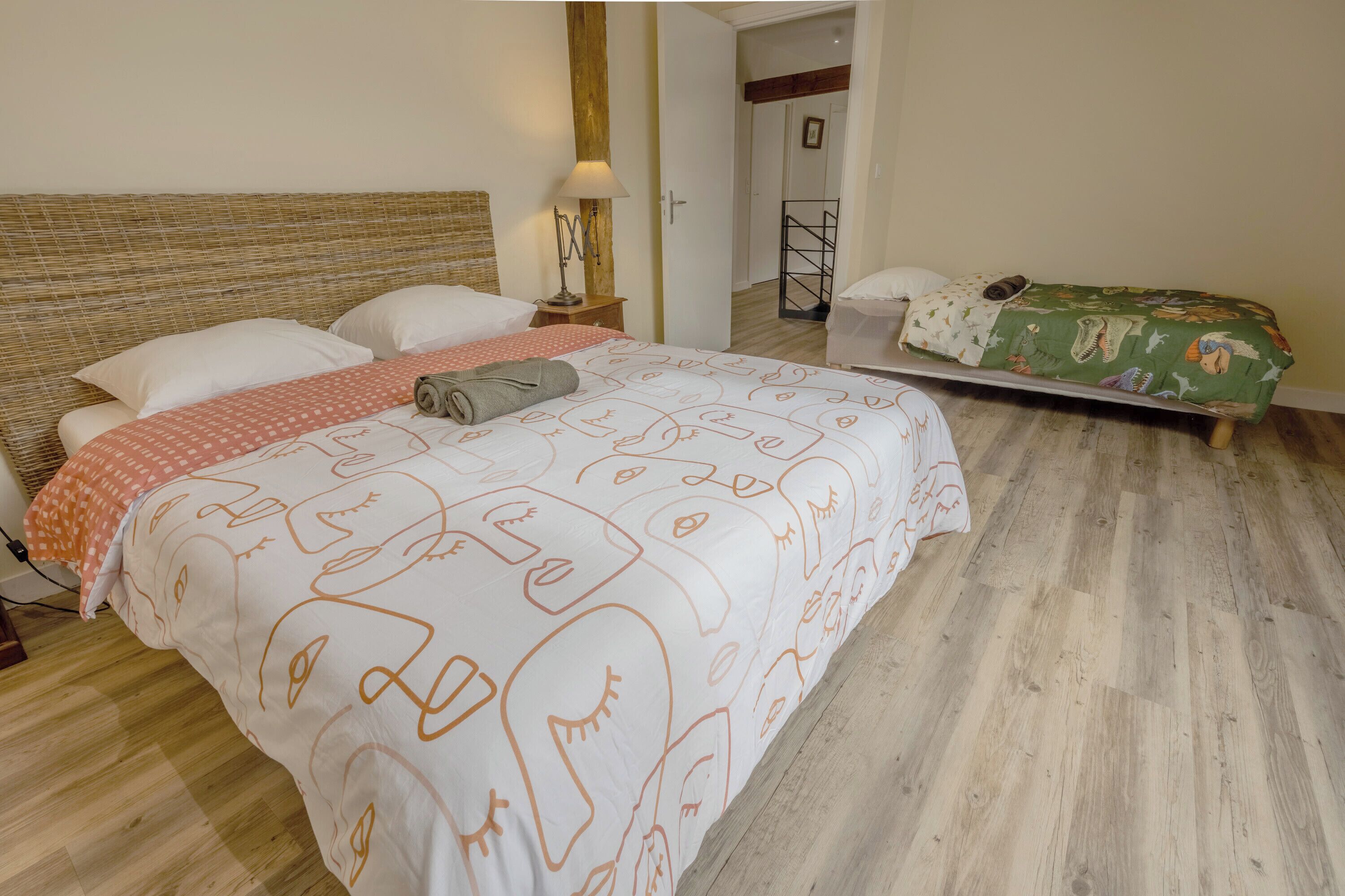 A bedroom with a large bed, a smaller bed, a nightstand, and a lamp.
