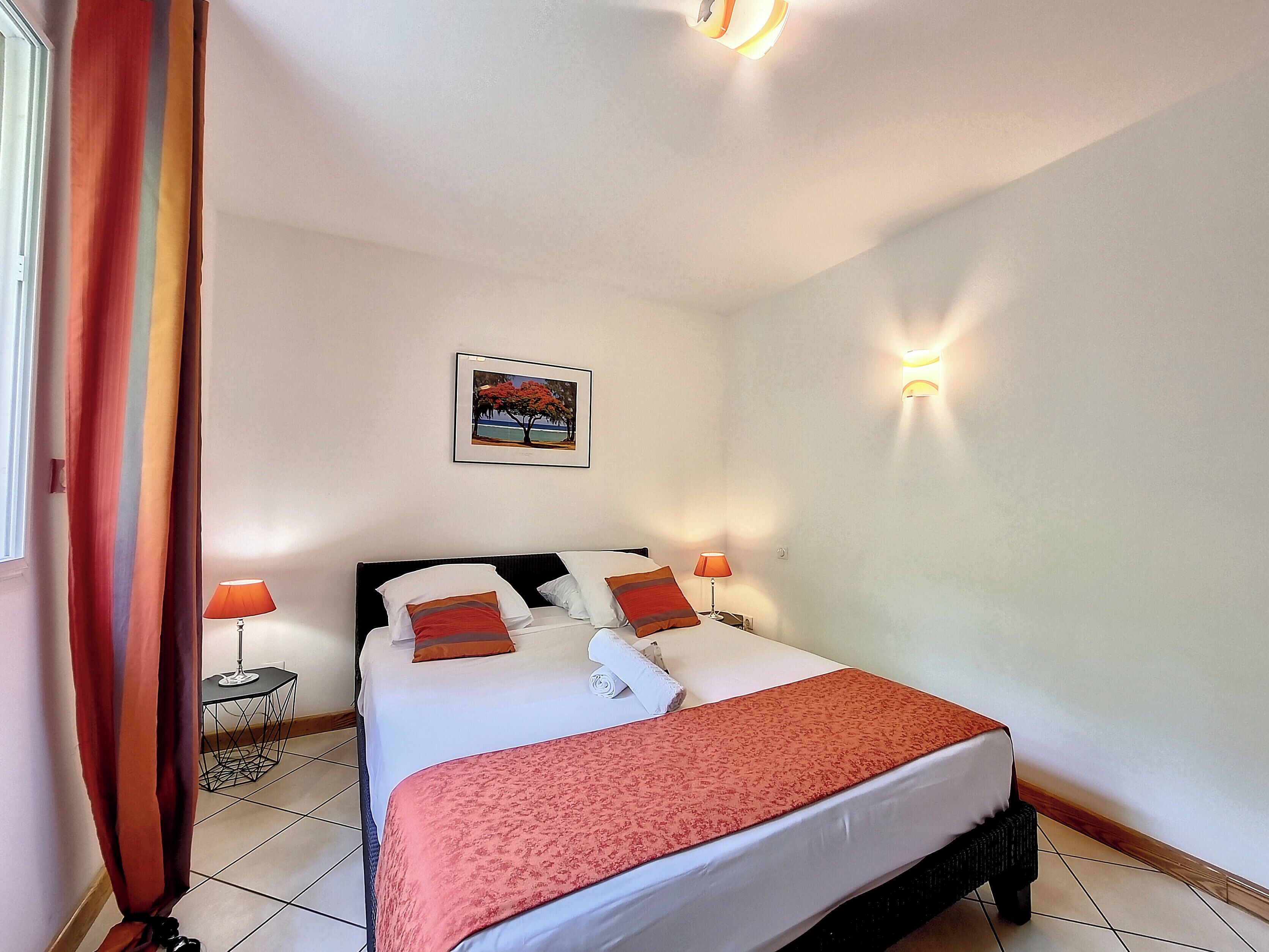Quarto de hotel com uma cama, duas luminárias de cabeceira, um quadro na parede e uma janela com cortinas.