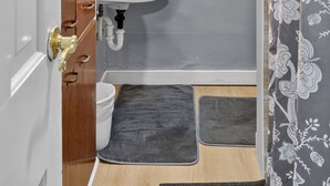 A compact bathroom with a white sink, wooden cabinet, and a shower curtain with a floral pattern. - Cozy Private Home w Fire Pit Near Downtown! (Kalamazoo)