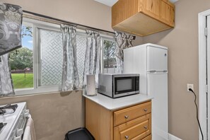 Eine kleine Küche mit Mikrowelle, Kühlschrank, Holzschrank und einem Fenster mit Vorhängen.