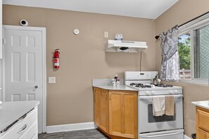 Una cocina funcional con estufa blanca, armarios de madera y una ventana con cortinas.