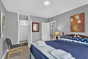 Ein Hotelzimmer mit Bett, Sessel, Tür, Gemälde und Lampe.
