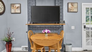 A dining area with a brick fireplace, a flat-screen TV mounted above a wooden table, and two chairs. - Cozy Private Home w Fire Pit Near Downtown! (Kalamazoo)