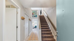 A hallway with a carpeted staircase, a door with a latch, and a wall-mounted artwork. - Coastal Sea Palms Retreat | Golf Views + Screened Porch (Saint Simons Island)