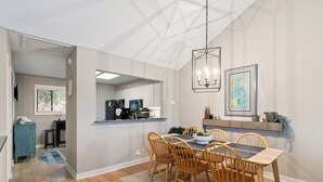 A dining area with a wooden table and chairs, a chandelier, and artwork on the wall. - Coastal Sea Palms Retreat | Golf Views + Screened Porch (Saint Simons Island)