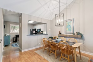 A dining area with a wooden table and chairs, a chandelier, and artwork on the wall. - Coastal Sea Palms Retreat | Golf Views + Screened Porch (Saint Simons Island)