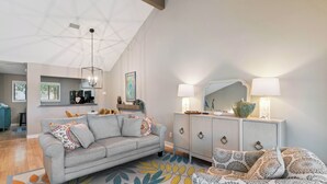 A modern living room with a sofa, a patterned rug, a cabinet with a mirror, and a ceiling with a geometric design. - Coastal Sea Palms Retreat | Golf Views + Screened Porch (Saint Simons Island)