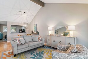 A modern living room with a sofa, a patterned rug, a cabinet with a mirror, and a ceiling with a geometric design. - Coastal Sea Palms Retreat | Golf Views + Screened Porch (Saint Simons Island)