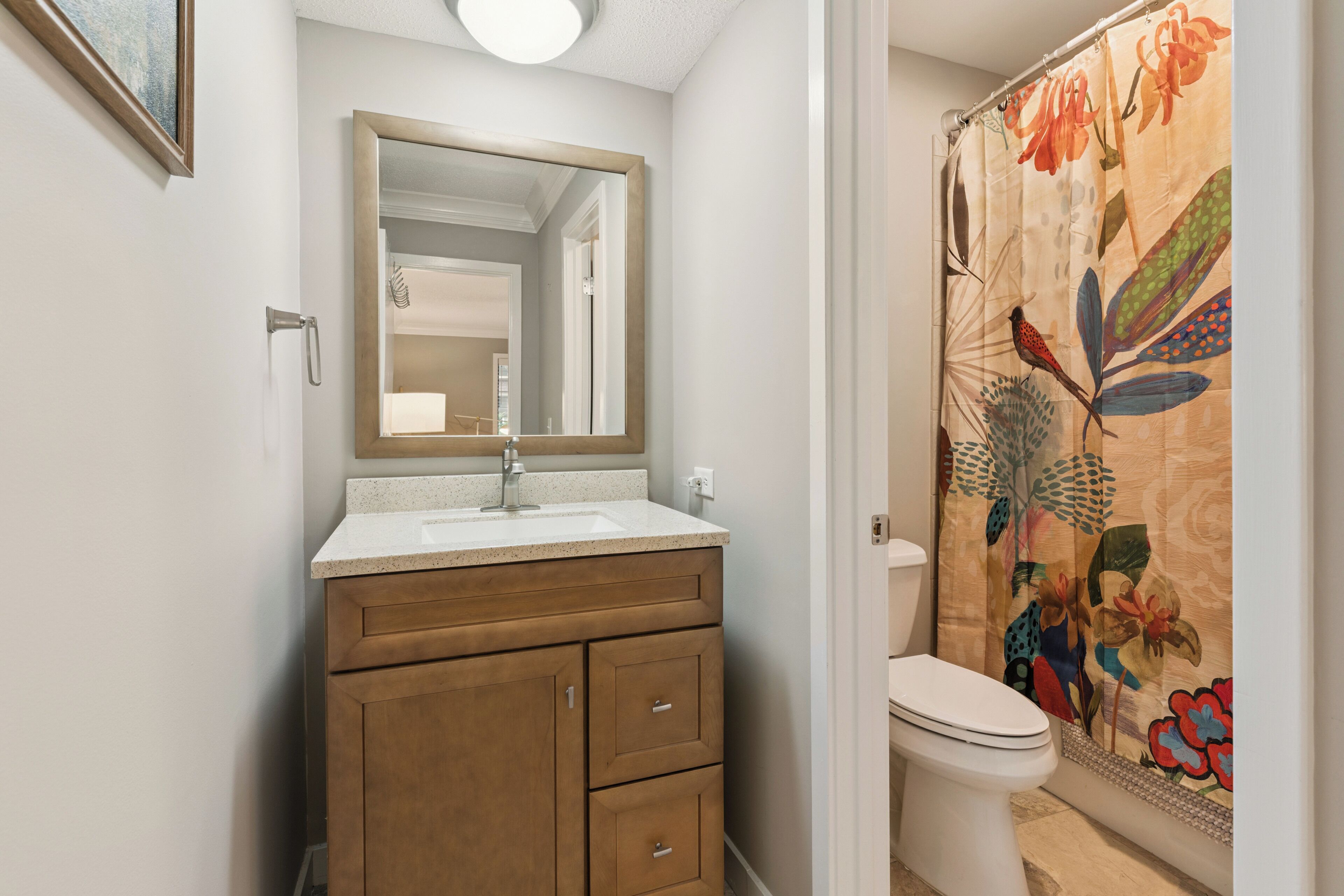 A bathroom with a wooden vanity, a white sink, a mirror, a toilet, and a shower curtain with floral patterns.