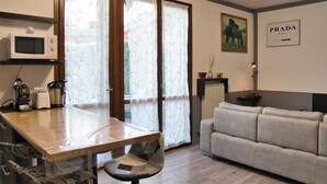 Une cuisine équipée d’un four à micro-ondes, d’un grille-pain et d’une machine à café, une table à manger avec une chaise, un canapé et une fenêtre avec des rideaux.