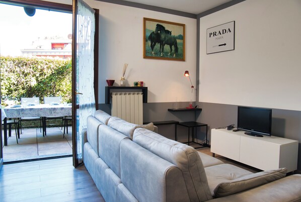 Un salon moderne avec un canapé, un téléviseur posé sur un meuble, un tableau et un panneau indiquant la direction à suivre pour se rendre chez Prada.