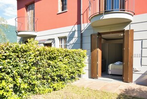Un hôtel avec un balcon, un lit recouvert d’une couverture blanche et une porte en bois.