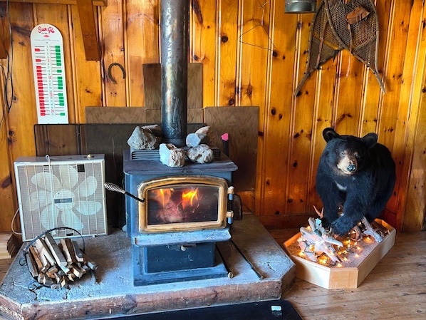 Ein Kaminofen mit Holzscheiten, eine Bärenfigur und ein Thermostat an einer Holzwand.