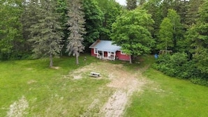 A red house with a porch, surrounded by trees and a grassy yard. - Rustic Fishing Lodge located on the Main Southwest Miramichi (Bloomfield Ridge)
