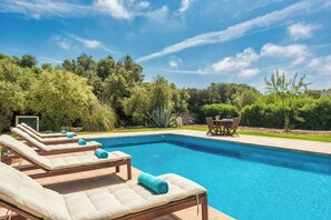 A swimming pool with lounge chairs and a table, surrounded by greenery.