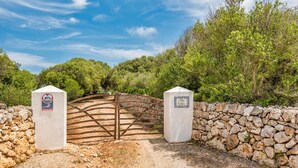 A rustic stone wall with a wooden gate leading into a wooded area. - Villa Mig Coster - A rural retreat on a private estate (Sant Lluís)
