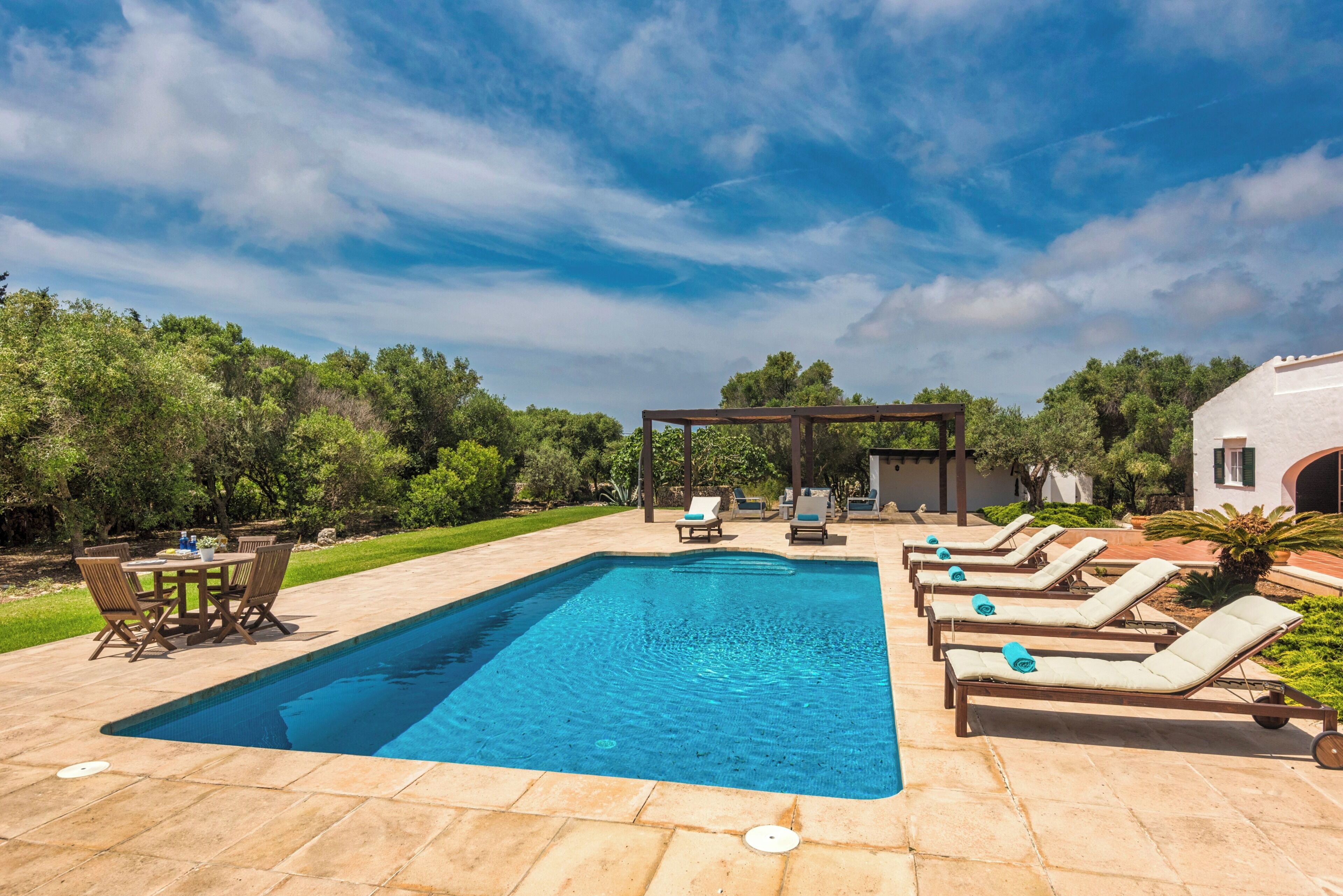 Une piscine rectangulaire, agrémentée de chaises longues et d’une pergola, dans un espace extérieur aménagé.