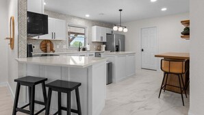 A modern kitchen with white cabinetry, a central island with stools, a built-in oven, and a refrigerator. - Keystone Lake Getaway (Sand Springs)