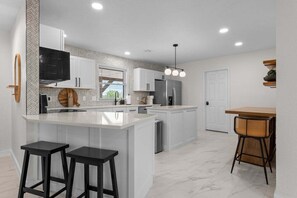 A modern kitchen with white cabinetry, a central island with stools, a built-in oven, and a refrigerator. - Keystone Lake Getaway (Sand Springs)
