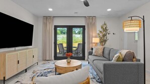 A modern living room with a sofa, a round coffee table, a television, and a ceiling fan. - Keystone Lake Getaway (Sand Springs)