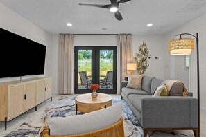 A modern living room with a sofa, a round coffee table, a television, and a ceiling fan. - Keystone Lake Getaway (Sand Springs)