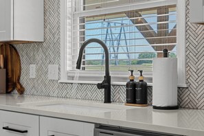 A kitchen with a modern faucet, two soap dispensers, and a window with blinds. - Keystone Lake Getaway (Sand Springs)