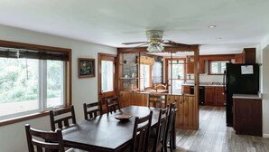 A kitchen with wooden cabinets, a dining table with chairs, a ceiling fan, and a view of the outdoors. - Scenic Wine Trail Lodge w/ Decks & Lake Views (Penn Yan)