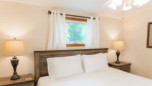 A bedroom with a wooden headboard, two bedside lamps, a window with curtains, and a nightstand with a lamp. - Scenic Wine Trail Lodge w/ Decks & Lake Views (Penn Yan)