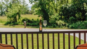 A bottle of wine and a glass on a railing with a view of a road and greenery. - Scenic Wine Trail Lodge w/ Decks & Lake Views (Penn Yan)