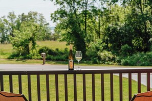 A bottle of wine and a glass on a railing with a view of a road and greenery. - Charming Wine Country Lodge with Scenic Views (Penn Yan)