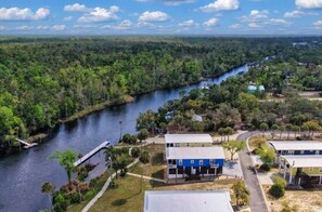 A river with a bridge, surrounded by dense forest, and a row of buildings with a dock. - The Blue Heron at River's Bend - Steinhatchee (Steinhatchee)