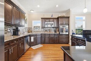 A modern kitchen with dark wood cabinets, granite countertops, stainless steel appliances, and a wooden floor. - The Blue Heron at River's Bend - Steinhatchee (Steinhatchee)