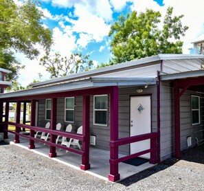 Ein kleines, eingeschossiges Motel mit überdachter Veranda und weißen Plastikstühlen.
