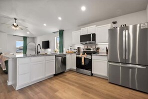 A modern kitchen with white cabinets, stainless steel appliances, a dishwasher, and a ceiling fan. - The Sage - 3BR/2BA - New Construction (Lubbock)