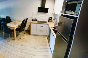 Eine kompakte Küche mit Esstisch, Stühlen, einer Mikrowelle, einer Kaffeemaschine und einem Kühlschrank.
