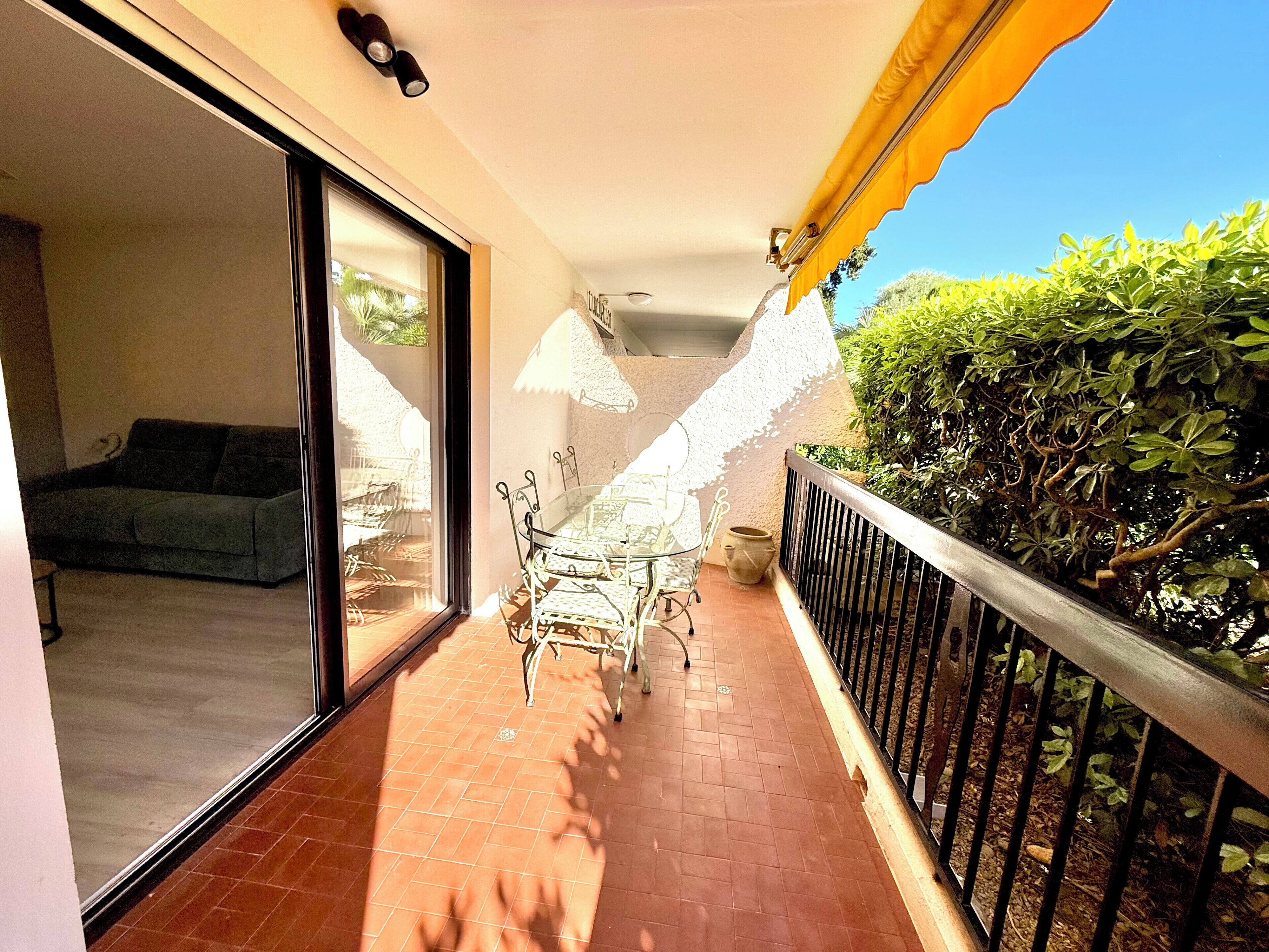Un balcon doté d’un sol carrelé, une porte vitrée donnant sur une pièce, une petite table avec des chaises et une rambarde en métal.