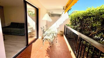 Un balcon doté d’un sol carrelé, une porte vitrée donnant sur une pièce, une petite table avec des chaises et une rambarde en métal.