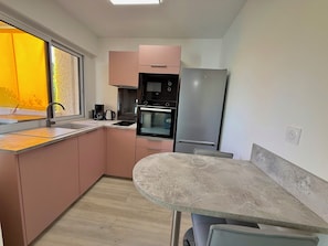 Eine moderne Küche mit rosafarbenen Schränken, einem Edelstahlkühlschrank, einem Einbauofen und einem Fenster mit Blick auf Bäume.