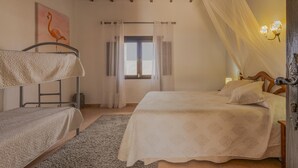 Quarto com teto de madeira, cama com dossel, mesa de cabeceira, luminária fixada na parede e cortinas na janela.