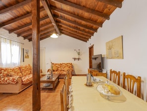 Un salon chaleureux avec un plafond en bois, un canapé, une table à manger avec des chaises et un téléviseur.