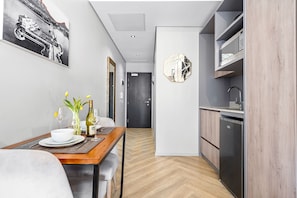 A modern kitchen with a built-in dishwasher, a dining area with a table set for two, and a hallway leading to a door. - One Thibault 1609 - Studio Apartment, Sleeps 2 (Cape Town)