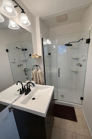 Een moderne badkamer met een douchecabine van glas, een wit wastafelmeubel met zwarte kraanwerk en een spiegel boven het wastafelmeubel.