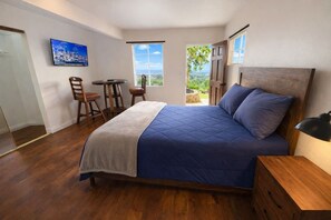 Een slaapkamer met een bed, een bureau en een stoel. Er is een raam met uitzicht op groen.