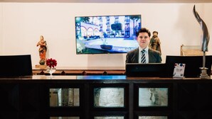 A reception desk with a television displaying a hotel interior, a statue, and a decorative lamp. - Best Western San Pedro Puebla (Puebla)
