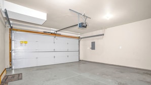 Eine Garage mit weißer Rolltür, einem an der Decke befestigten Projektor und einem Betonboden.