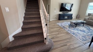 A staircase leading to a living room with a flat-screen TV, a sofa, and a coffee table.
